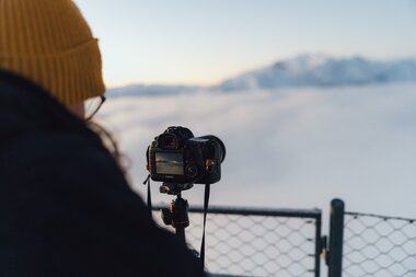 Person taking photos of a snowy mountain landscape with a camera on a tripod. | © Evolumina