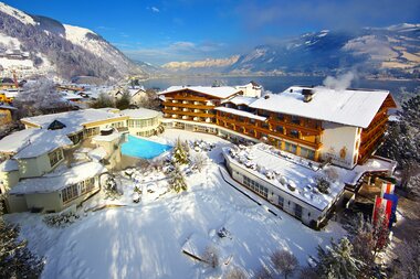 Snow-covered resort with multiple buildings and a pool in a mountain landscape during winter. | © Salzburgerhof Zell am See
