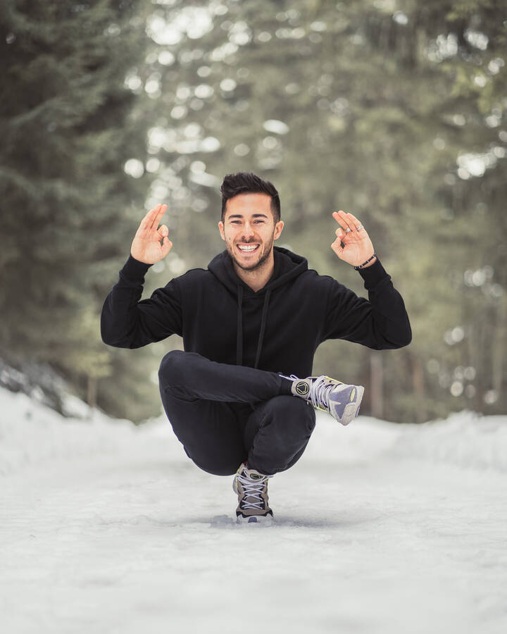 Person in a squat position in a snowy winter landscape, smiling with raised hands. | © Katharina Eder Arts 