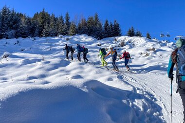 Groups of winter sports enthusiasts on a snowy mountain landscape, some with skis, under a clear blue sky. | © Marc Stickler Photography