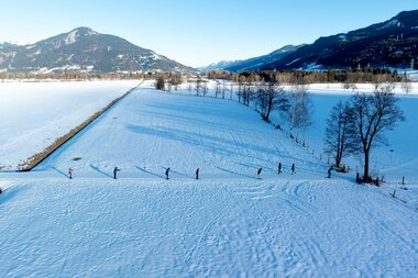 Snow-covered landscape with trees, mountains in the background, and a clear sunny sky. | © Marc Stickler Photography