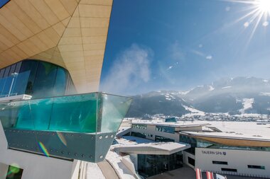 Modern hotel architecture with glass balcony overlooking snow-covered mountains under a blue sky | © Alexander, Maria Lohmann