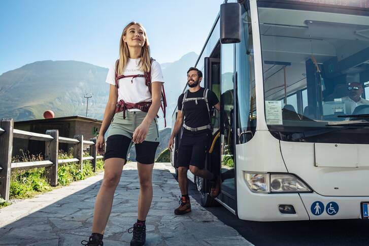 Travelers disembark from a bus to start a hike amidst mountain scenery. | © Zell am See-Kaprun Tourismus