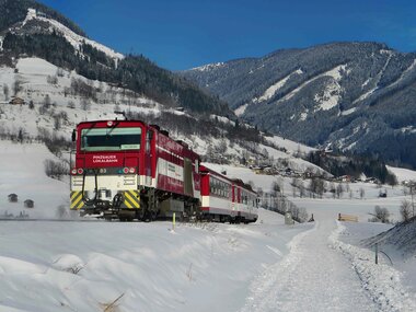 A train of the Pinzgauer Lokalbahn travels through a snowy winter landscape in the mountains. | © Salzburg AG