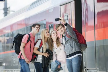 Group of young people taking a selfie at the train station in front of a train. | © Harald Eisenberger 