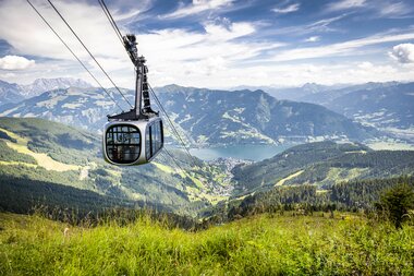 Cable car flying over green hills with a view of a lake and mountain landscape. | © Max Steinbauer