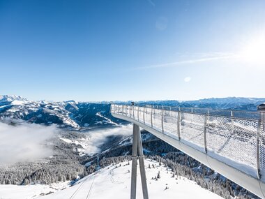 Viewing platform on a suspension bridge over snowy mountain landscape with clouds. | © Schmittenhöhebahn AG, Johannes Radlwimmer