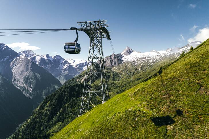 Cable car and cabin in a mountain landscape with mountains in the background and a green hillside. | © Kitzsteinhorn 