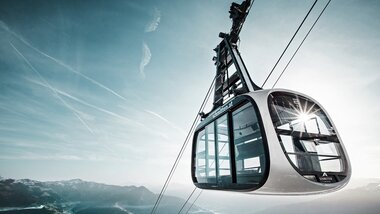 Cable car over mountain landscape illuminated by sunlight, ascending high in the mountains. | © Schmittenhöhe