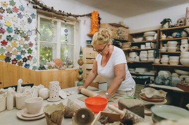 A person working in a ceramics studio, surrounded by pottery and tools. | © Zell am See-Kaprun Tourismus