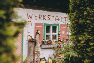 Small, colorful building with wall art and decorations, surrounded by greenery, viewed through trees. | © Zell am See-Kaprun Tourismus