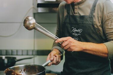 A chef cooking in a kitchen, smiling and focused while frying in a pan. | © Zell am See-Kaprun Tourismus