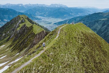Panoramic view of green mountain ridges with hikers on a narrow trail in the Kitzsteinhorn mountain range. | © Kitzsteinhorn