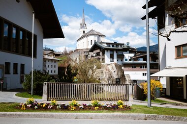 Typical Austrian village with church on a rock in spring, colorful flower bed in front of the street.