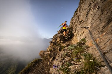 Person climbing a steep rock face in the mountains on a sunny day. | © MarkusFruehmann