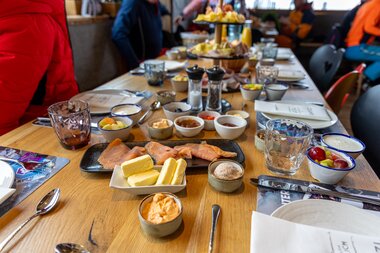 A well-set breakfast table with various foods, turquoise and clear glasses, colorful dishes and cutlery, in a cozy atmosphere. | © Wouter Hagen