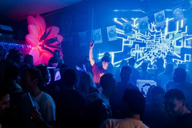 People dancing at a party with colorful lighting effects and a digital background. | © Tim Mengerink