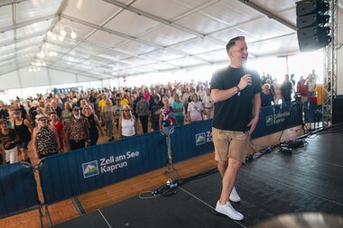 Host on stage at a line dance event inside a tent, with audience in the background. | © Zell am See-Kaprun, JOE