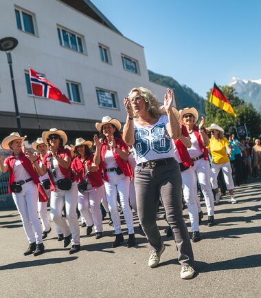 Festive parade with dancers in traditional costumes, accompanied by flags of various countries, on a street in an Alpine town. | © Zell am See-Kaprun, JOE