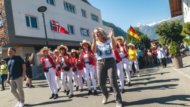 Festive parade with dancers in traditional costumes, accompanied by flags of various countries, on a street in an Alpine town. | © Zell am See-Kaprun, JOE