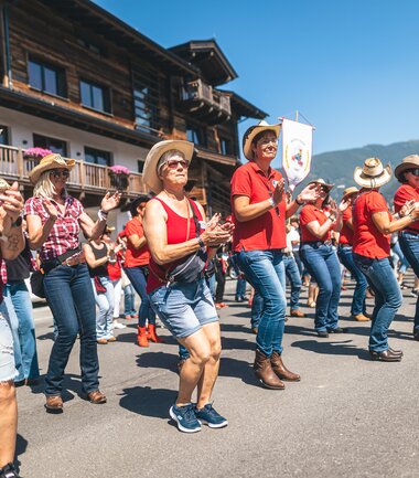 Participants line dancing at the AlpFestival 2025 outdoors in front of traditional buildings on a sunny day. | © Zell am See-Kaprun, JOE