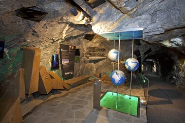 Exhibition in a cave featuring interactive globe-shaped models and informational displays. | © Kitzsteinhorn 