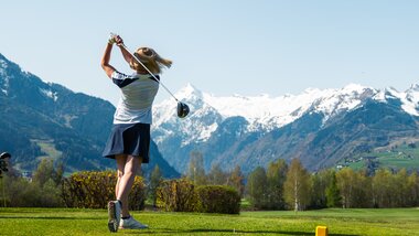 Person teeing off on a golf course with mountain peaks covered in snow in the background. | © Zell am See-Kaprun Tourismus
