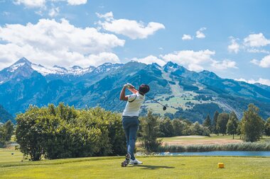 Golfer taking a shot on a golf course with mountain scenery in the background. | © Johannes Radlwimmer