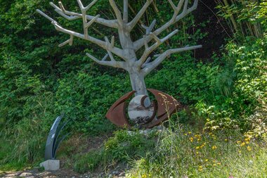 Metal tree sculpture in a green garden with bushes and flowers. | © Edith Danzer