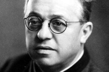 Black and white photo of a person with round glasses, short hair, and formal attire.