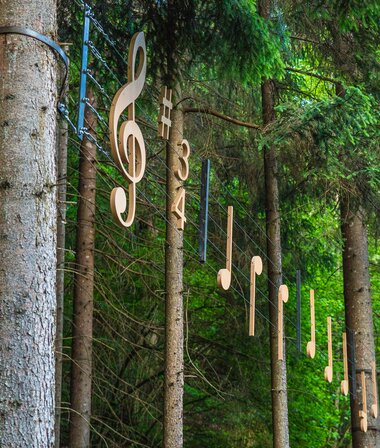 Sound sculpture with music notes attached to trees in a forest.