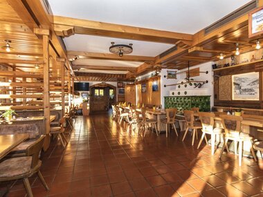 Cozy interior of a rustic bar or restaurant with wooden decorations, tables, and chairs. | © Stangerbauer Kaprun