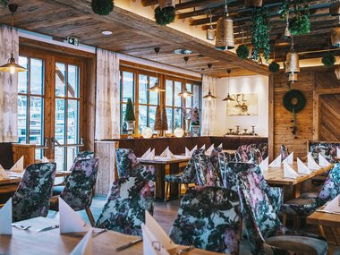 Cozy restaurant with large windows, set tables, colorful chairs, rustic wood decor, and festive decorations. | © Baumbar Kaprun