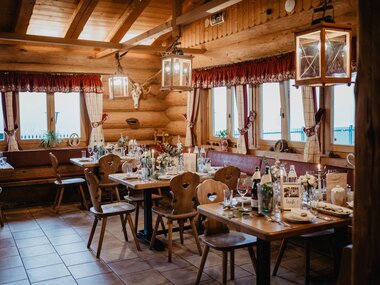 Cozy rustic interior of a cabin with wood, tables, chairs, candles, and decorations, ideal for a celebration. | © Jaga-Alm Zell am See