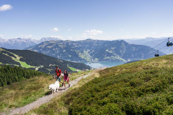 Hikers with a dog on a trail in the mountains with a view of Lake Zell and surrounding peaks | © Schmittenhöhe, Mr. Offenblende