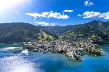 Aerial view of Zell am See with lake, town, and surrounding mountains on a sunny day. | © Nikolaus Faistauer