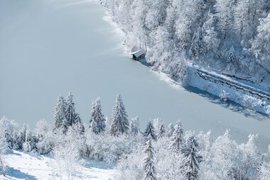 Winter landscape with snow-covered trees, a frozen lake, and a small cabin. | © Zell am See-Kaprun