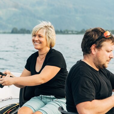 Two people fishing on a boat on Lake Zeller, surrounded by mountains and water. | © Zell am See-Kaprun Tourismus