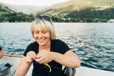 Person fishing on a boat on Lake Zeller with mountains in the background. | © Zell am See-Kaprun Tourismus