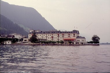 Historic photo of a hotel by a lake with mountains in the background.