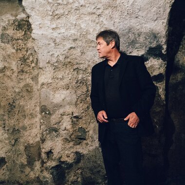 Person stands in front of an old, rocky wall, wearing dark clothing and looking to the right. | © Zell am See-Kaprun Tourismus