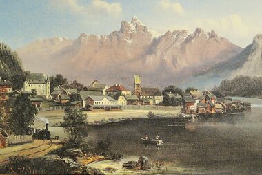 Scenic view of a town with buildings in front of mountain ranges, beside water with a boat.