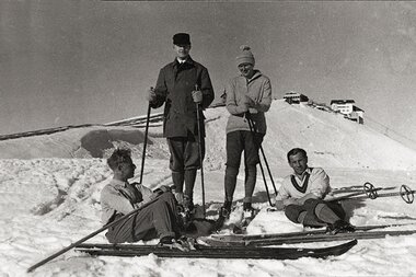 Historical black-and-white photo of people skiing on a snowy mountain with vintage skiing equipment.