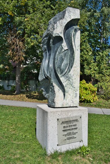 Stone sculpture with abstract, flowing shapes on a concrete pedestal in a park.