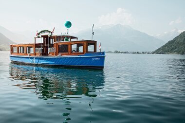A classic wooden boat on a calm lake with mountains in the background.