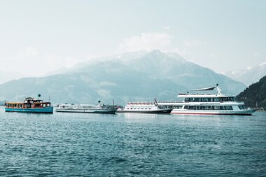 Several boats on a lake with mountains in the background on a sunny day.