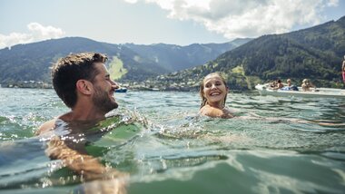 People swimming in the crystal-clear Zeller See with mountains in the background, laughing and having fun. | © Zell am See-Kaprun Tourismus