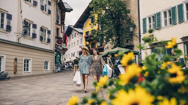 Pedestrians exploring the picturesque pedestrian street in Zell am See with colorful buildings and flowers in the foreground. | © Zell am See-Kaprun Tourismus