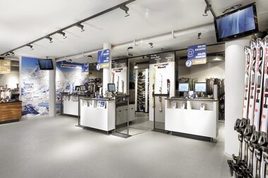 Ski and winter sports gear in a specialty shop, with skis, poles, and equipment displayed on the sales floor. | © Bründl Sports 
