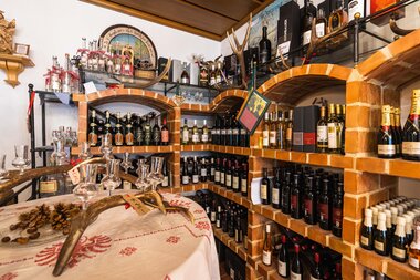 Shelf with wine bottles in a well-stocked wine shop, featuring wooden shelves and warm lighting. | © Johannes Radlwimmer